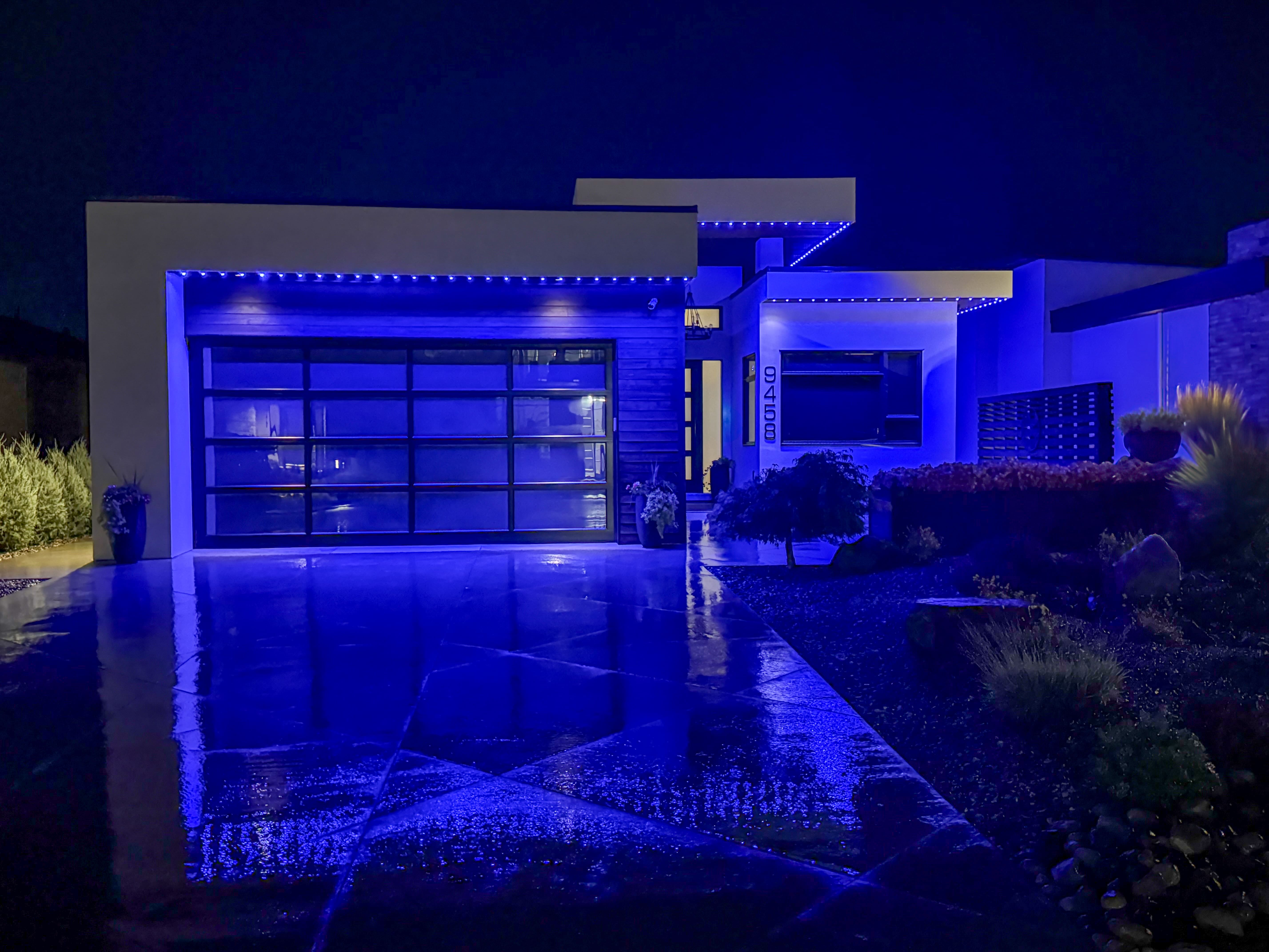 A modern home at night illuminated with sleek blue Perma-Lights along the roofline and garage, casting a cool, secure glow over the driveway and landscaped garden