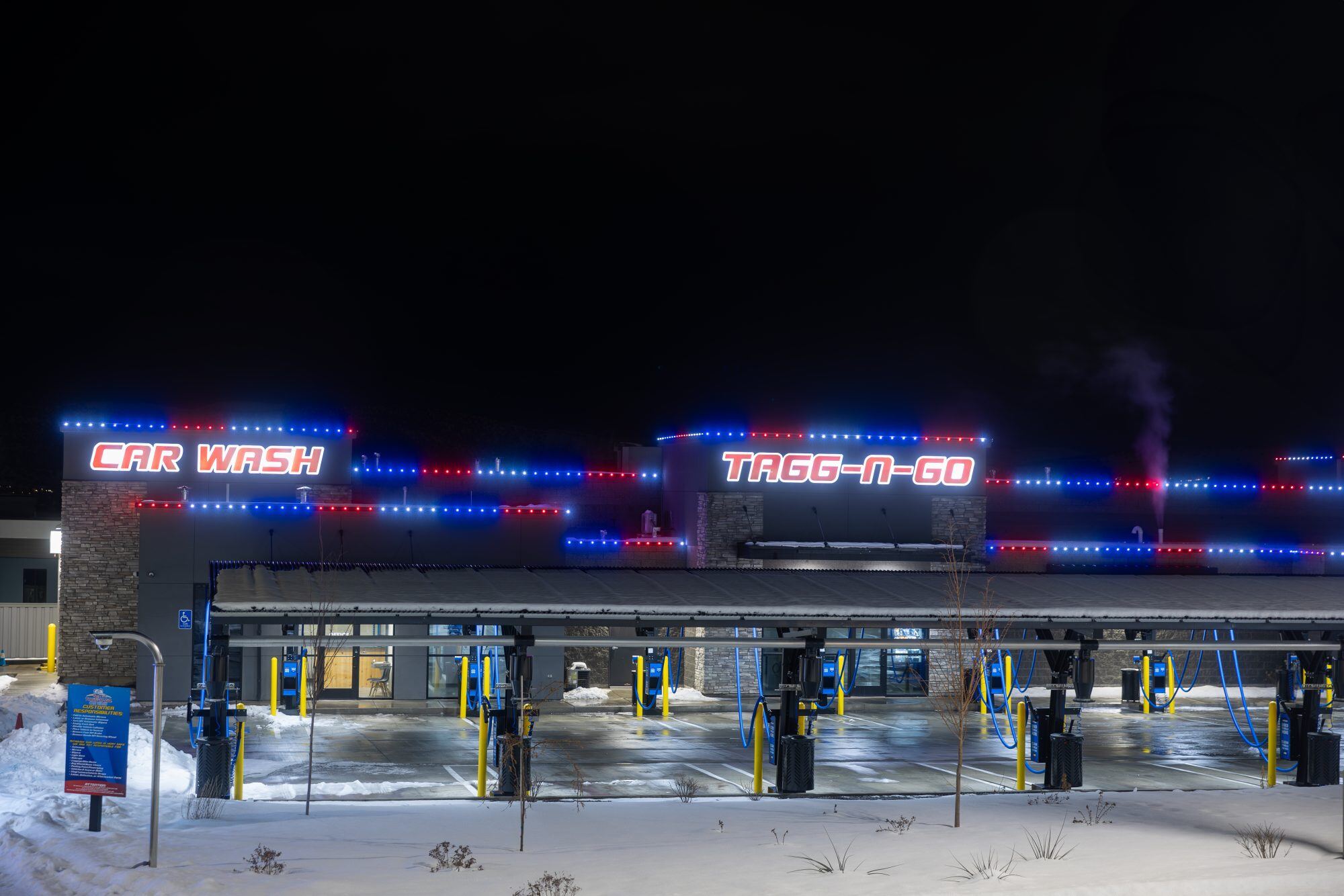 Commercial car wash building lit with red and blue permanent LED track lighting in winter nighttime setting