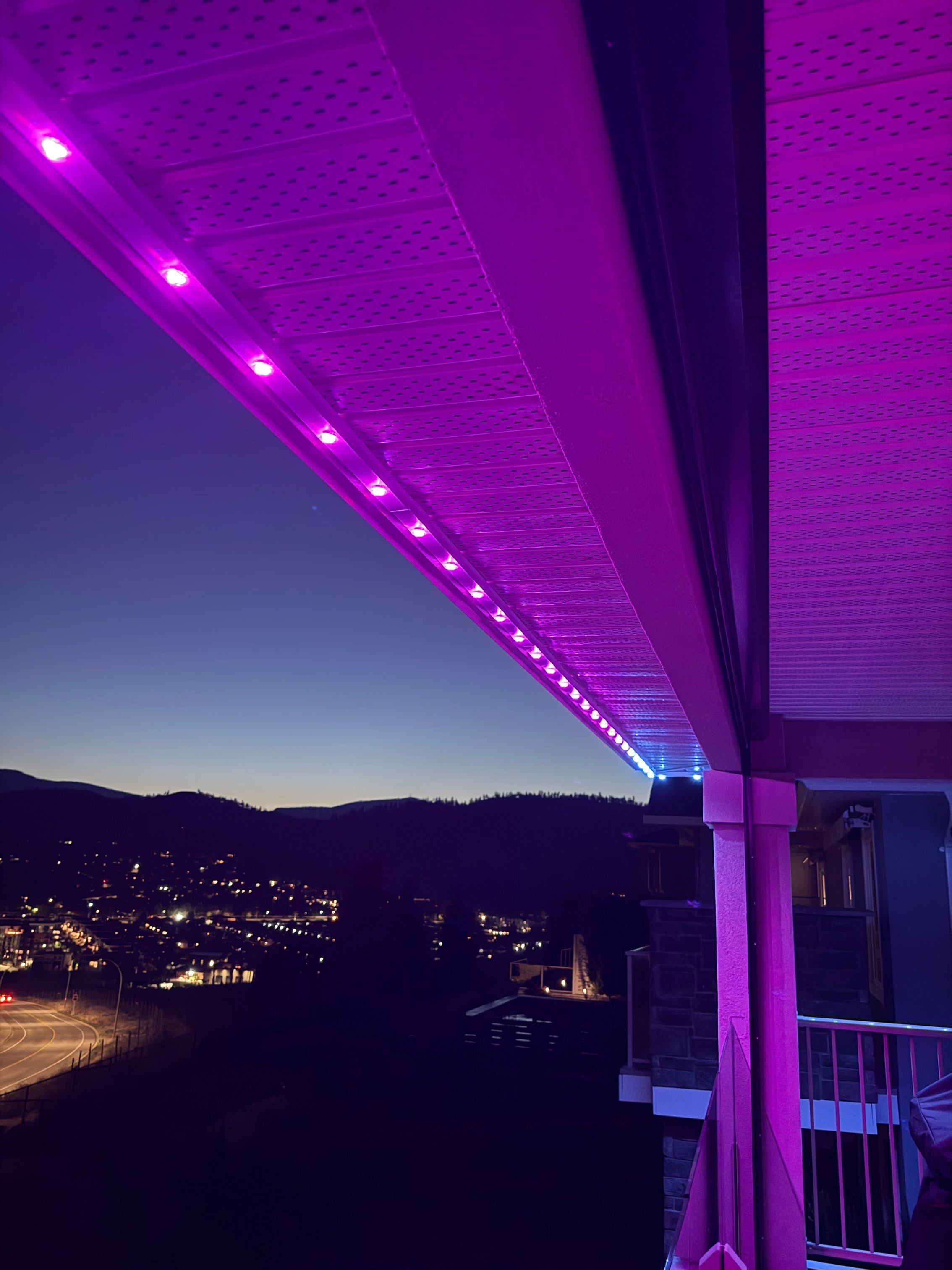 RGBW permanent patio lights on white aluminum track overlooking Kelowna cityscape at dusk