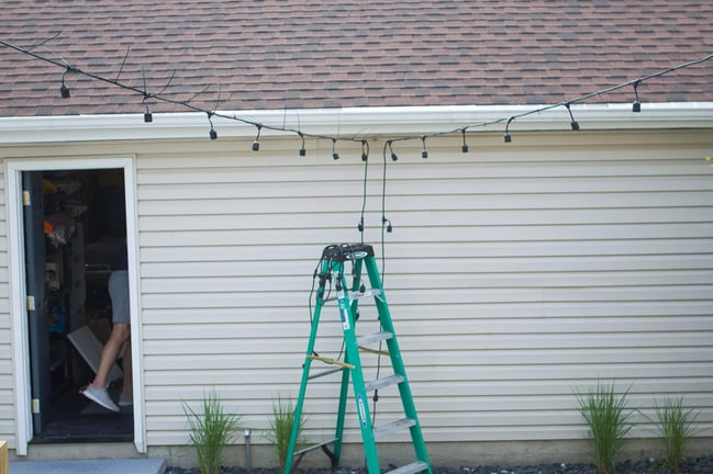 Improperly installed string lights with sagging cables, exposed wires, and unsecured power connections along a home’s roofline